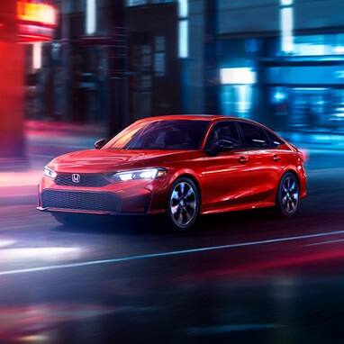 2027 Honda Civic Sedan Sport Touring Hybrid in Rallye Red front three-quarter view driving through a city (Compact Sedan)